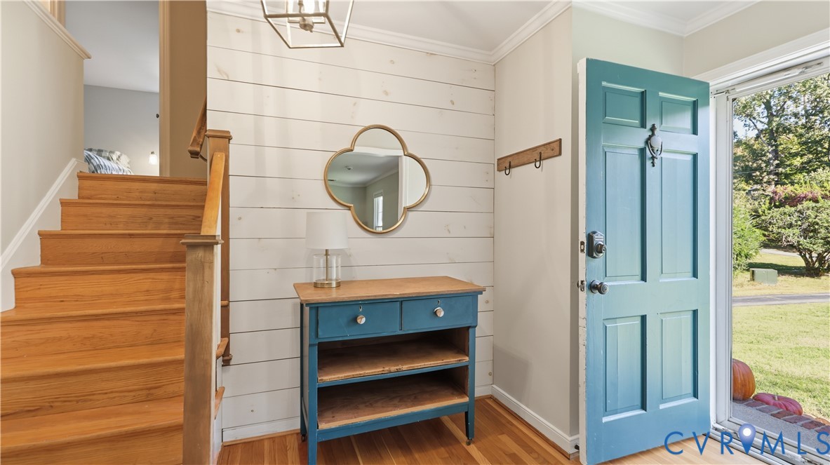 Foyer featuring horizontal shiplap wall paneling, natural wood-finish staircase with matching handrail, six-panel teal entry door, and geometric metal pendant lighting