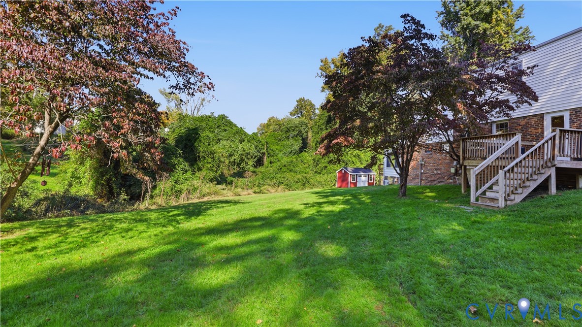 Expansive backyard featuring a large grass lawn, mature trees, wood-frame deck, and a detached storage shed