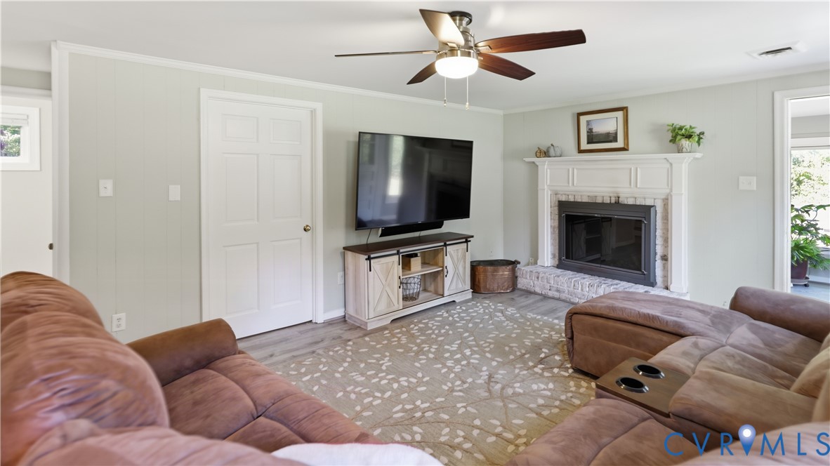 Living room featuring a fireplace with a white mantel and painted brick hearth, wood-finish flooring, and a ceiling fan with integrated lighting