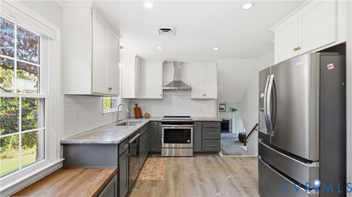 Kitchen featuring shaker-style cabinetry with dual-tone finish, stainless steel appliances, subway tile backsplash, stone-surface countertops, and wood-finish flooring