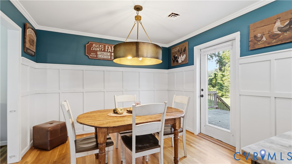 Dining area featuring wood-finish flooring, white board-and-batten wainscoting, a cylindrical metal pendant light, and a glass-paneled exterior door
