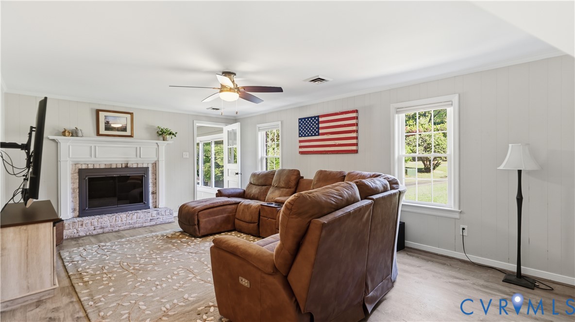 Living area featuring light wood-finish flooring, a brick fireplace with a decorative mantel, and a ceiling fan