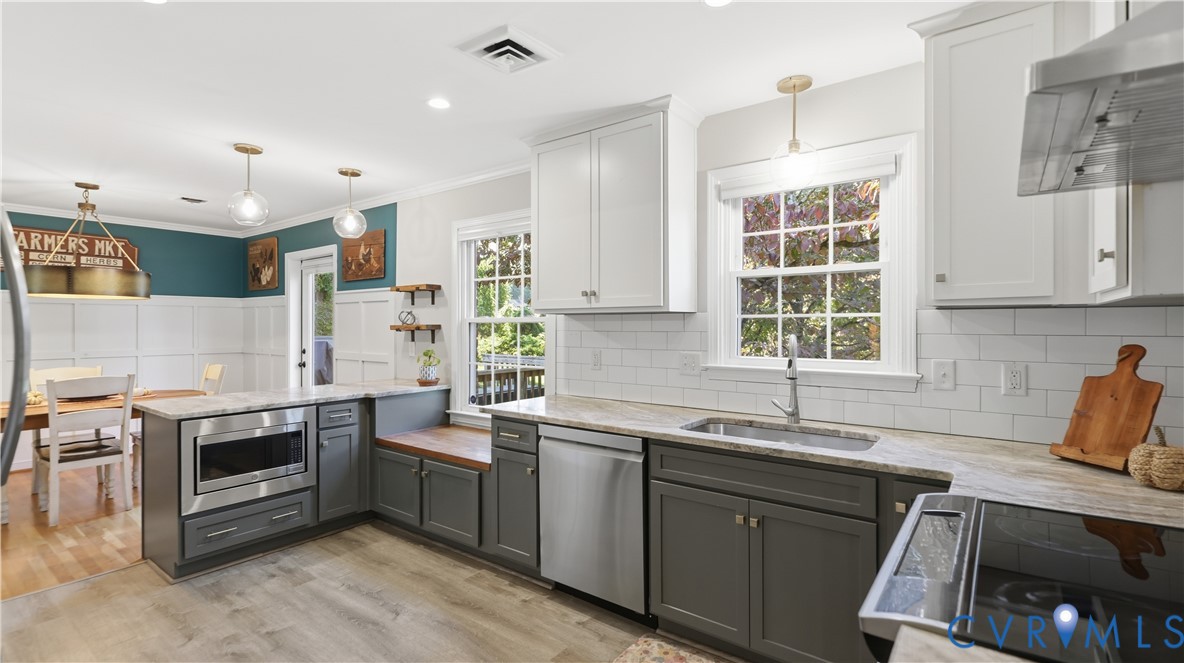 Kitchen featuring two-tone cabinetry, stone-finish countertops, stainless steel appliances, a white subway tile backsplash, and wood-finish flooring