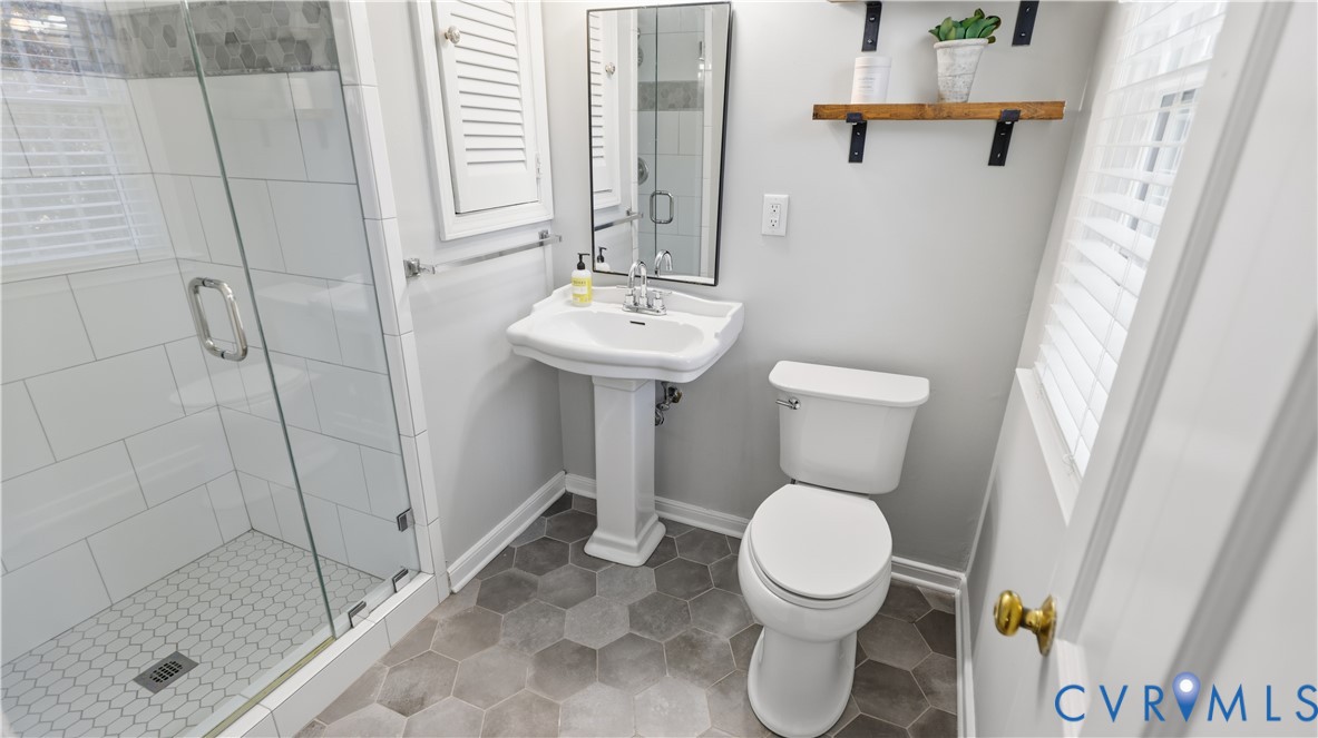 Glass-enclosed shower with white subway tile surround, pedestal sink, hexagonal tile flooring, and wall-mounted shelving