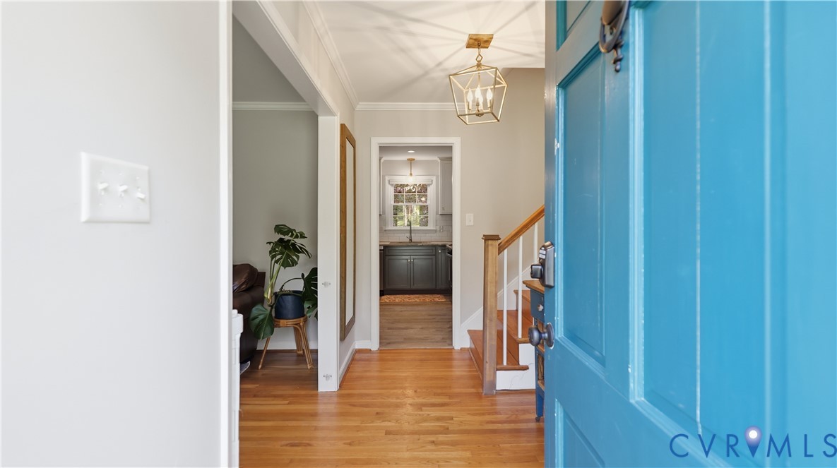 Entryway featuring wood-finish flooring, a metal geometric pendant light, and a painted wooden front door with a metal knocker
