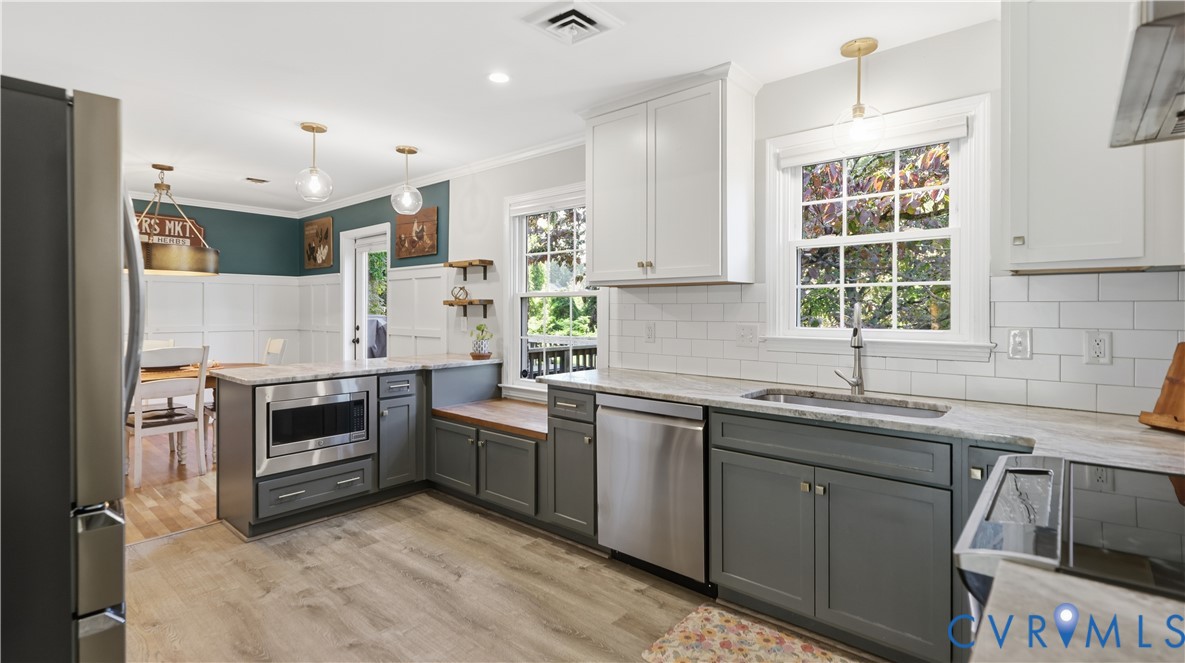 Kitchen featuring two-tone cabinetry, stone-finish countertops, white subway tile backsplash, stainless steel appliances, and wood-finish flooring