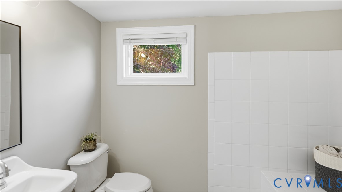 Wall-mounted mirror, pedestal sink with metal hardware, and white ceramic tile shower surround