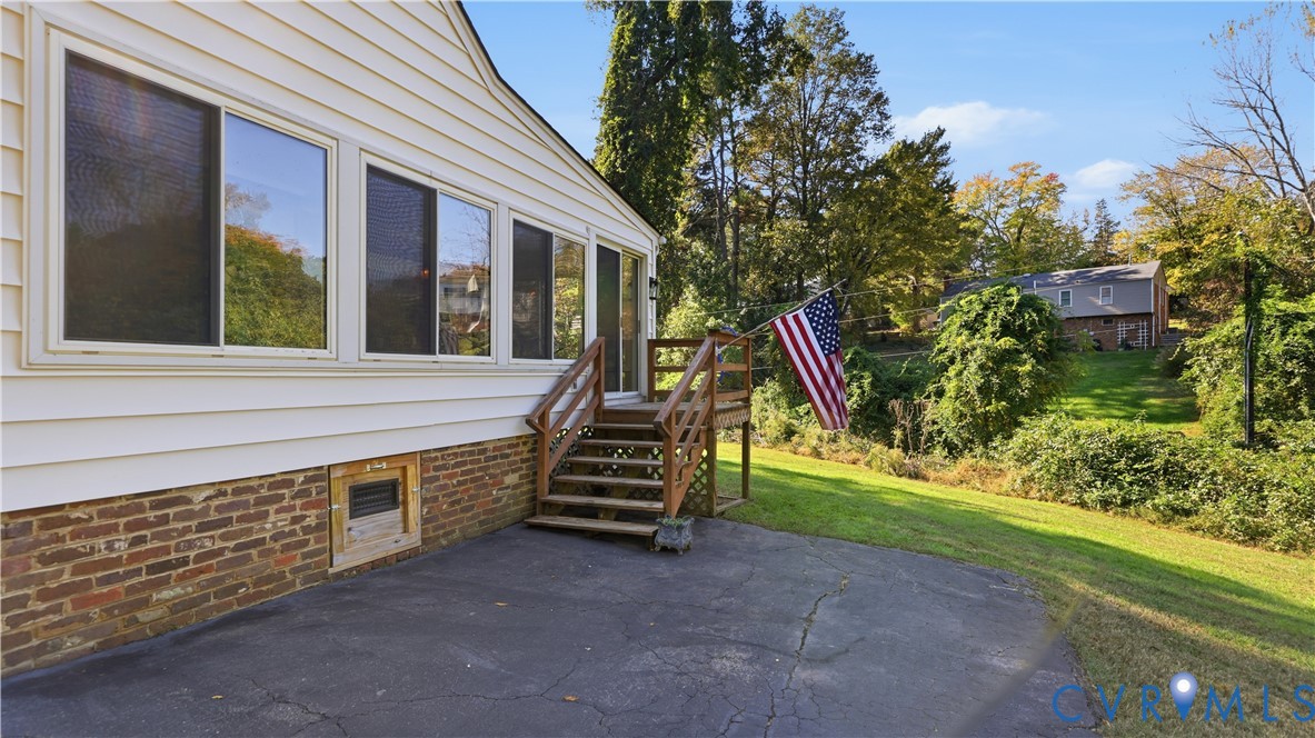 Exterior featuring horizontal siding, a red brick foundation base, a paved patio, and a raised wooden deck with stairs