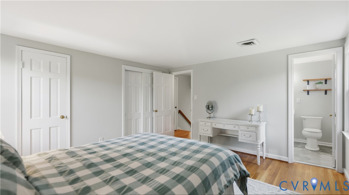 Bedroom featuring wood-finish flooring, multi-panel doors, bi-fold closet doors, and an attached bathroom with wall-mounted shelving
