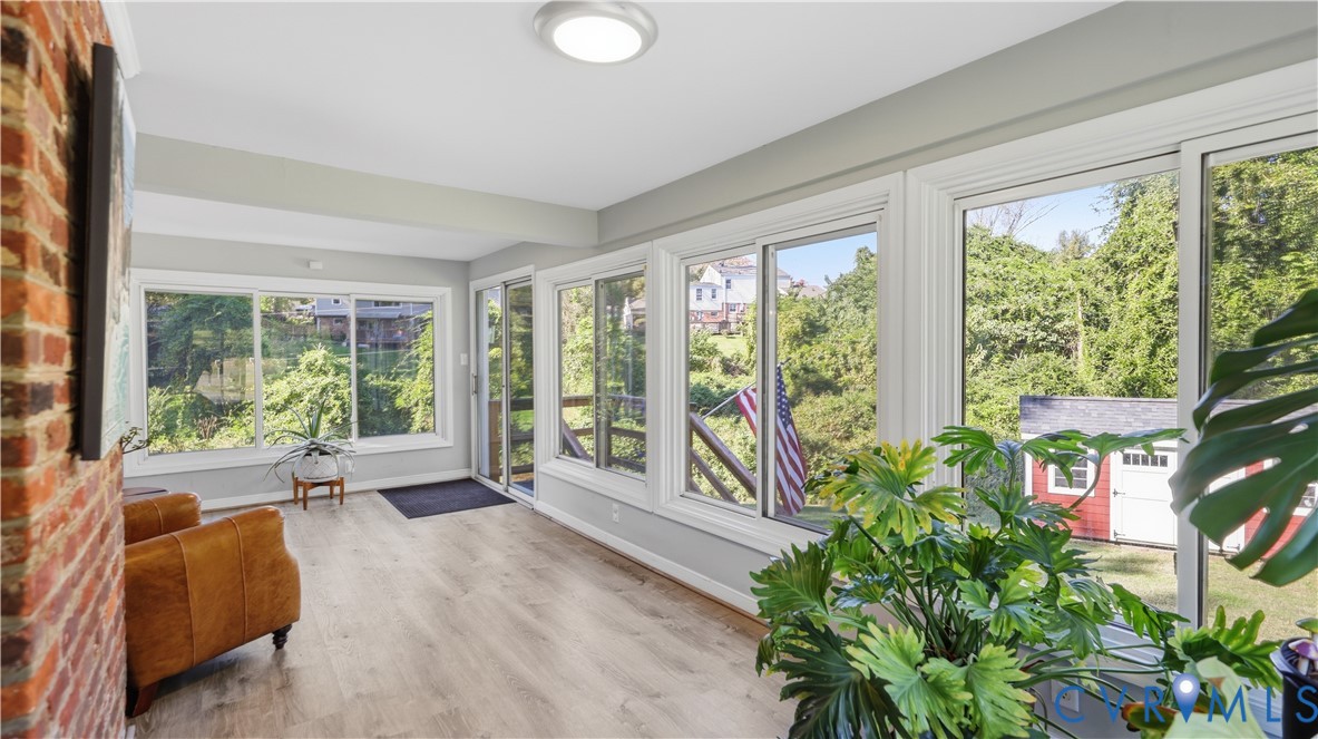 Sunroom featuring wood-finish flooring, extensive sliding windows, and an exposed brick accent wall