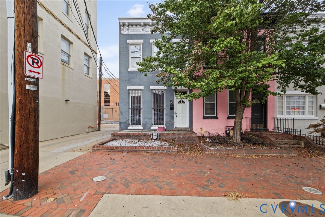 Two-story masonry townhouse exterior featuring a painted brick facade, raised brick-edged masonry planter beds, and decorative window lintels