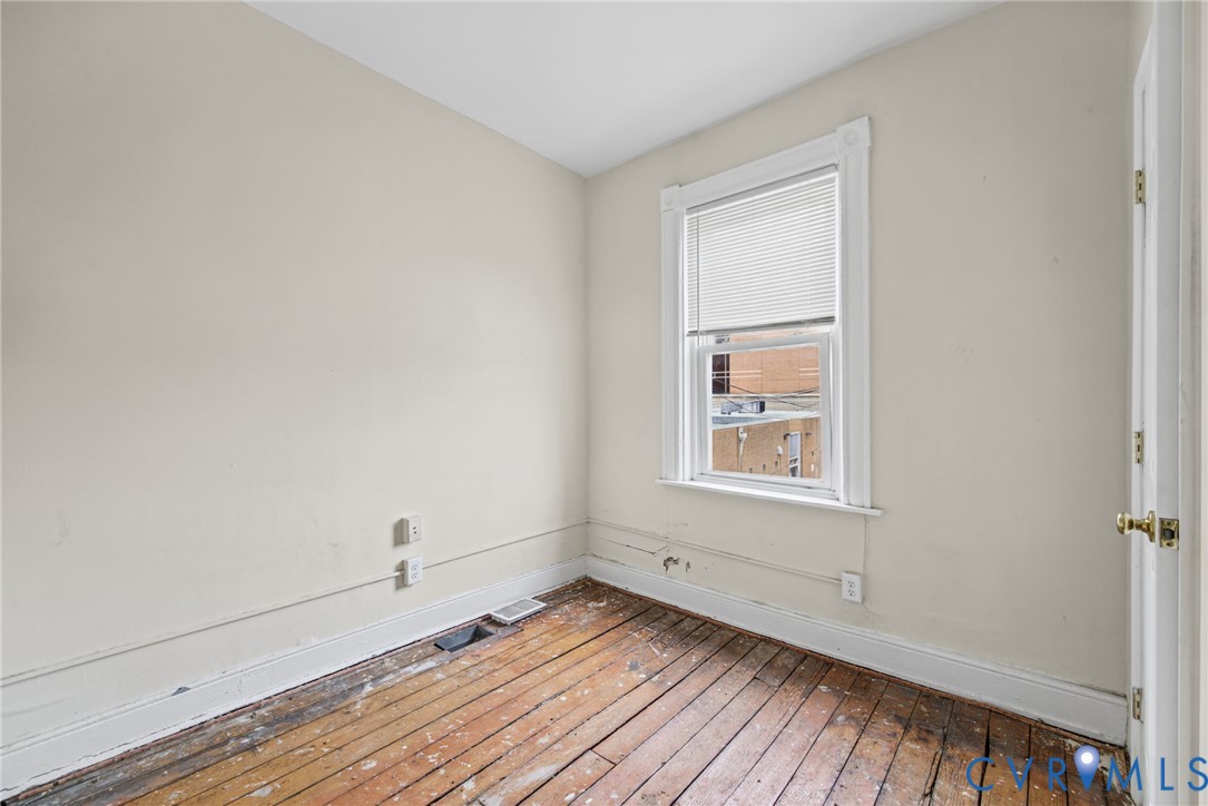 Bedroom 3 - Interior room featuring original wood-plank flooring, a single-pane window with white wood trim, and a classic hinged door with brass-finish hardware