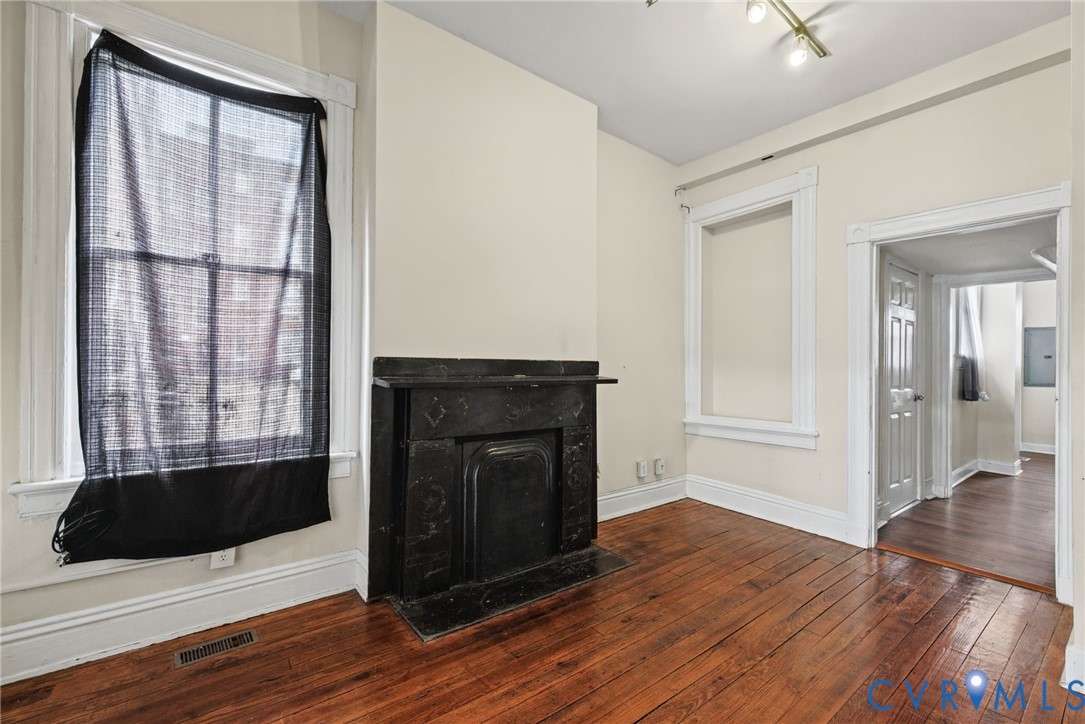 Wood-finish flooring, black hearth fireplace with mantle, and white window casing