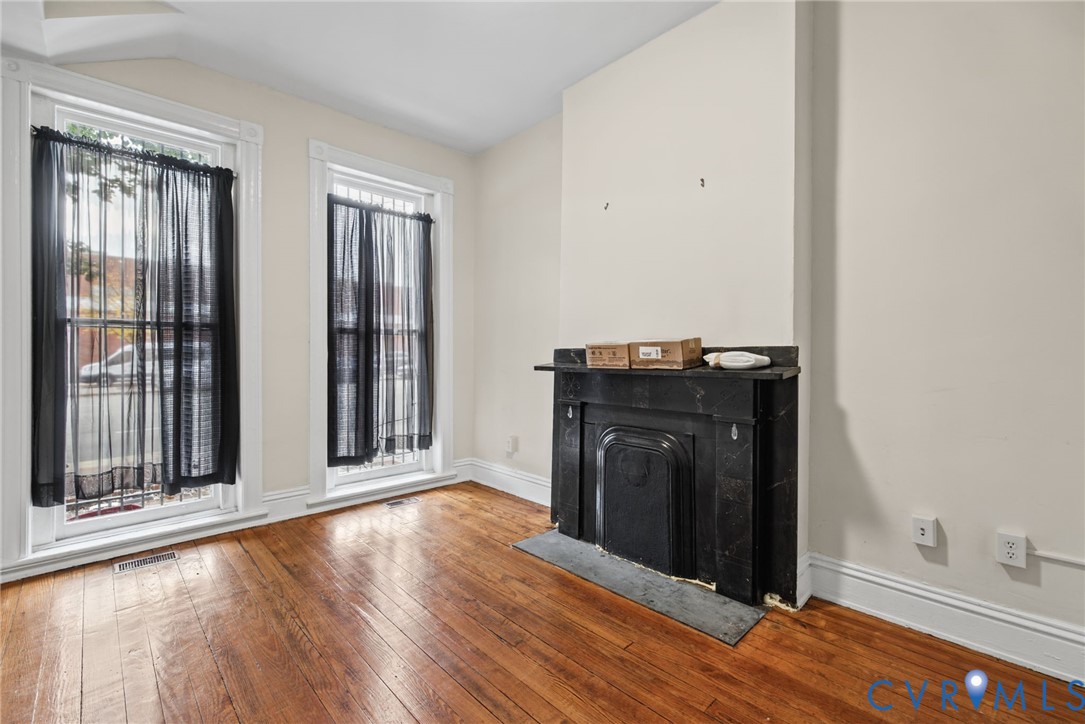 Interior space featuring hardwood flooring, two tall windows with decorative trim, and a dark stone fireplace mantel