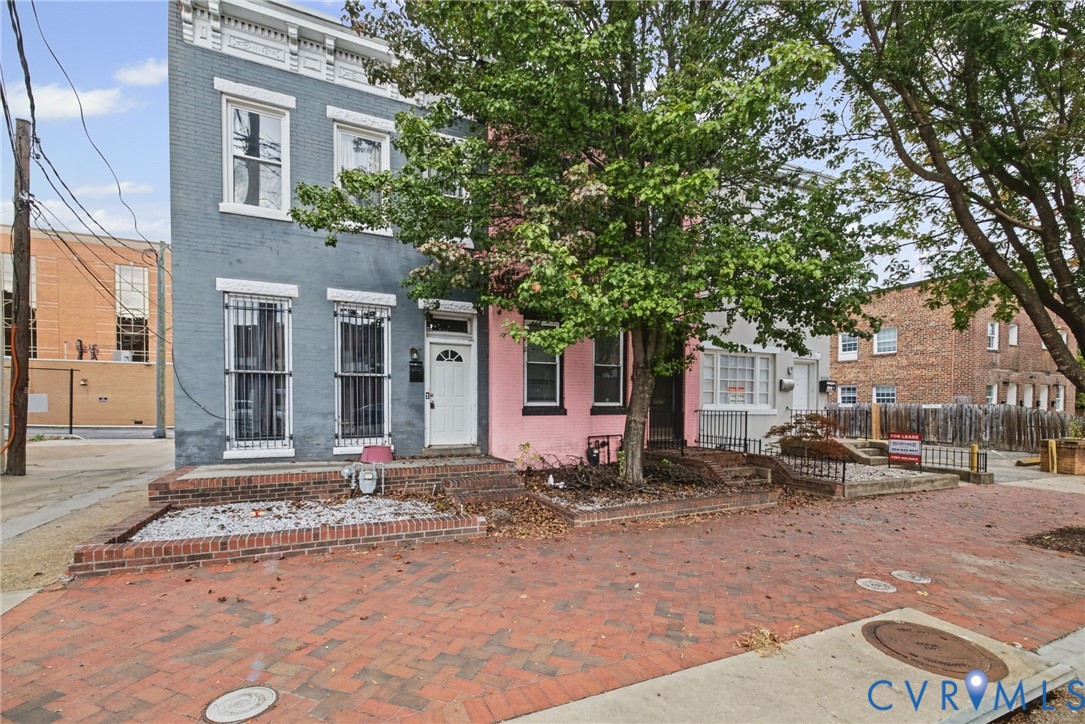 Multi-story masonry exterior featuring a painted brick facade, raised brick planter beds, and decorative window security bars