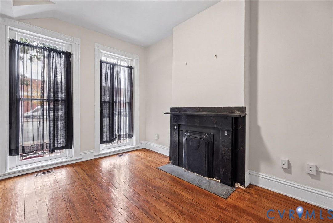 Bedroom 1 -Interior space featuring wood-finish flooring, high ceilings, dual tall windows, and a decorative fireplace with a stone mantel