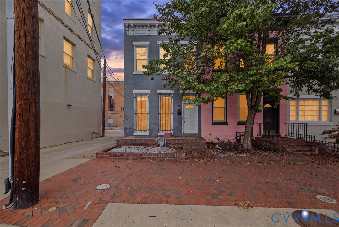Multi-story masonry exterior featuring vertical pane windows, decorative lintels, and a brick-paved front terrace with integrated planter beds