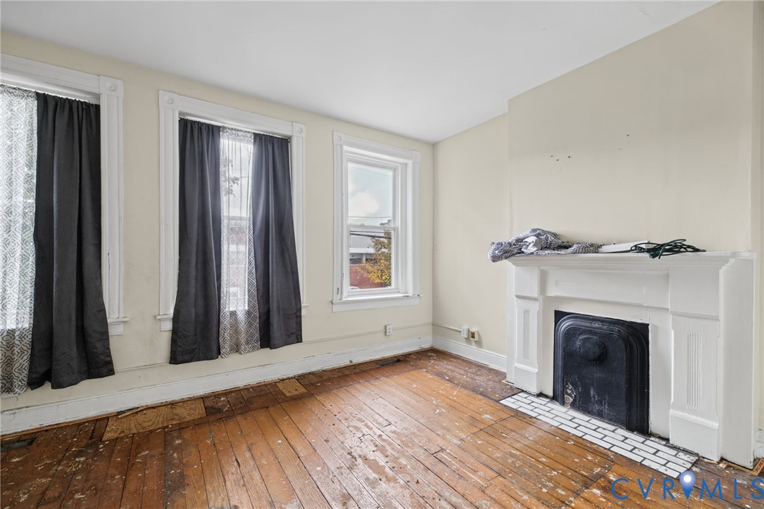 Interior room featuring natural wood flooring, a white fireplace mantel, a black metal firebox insert, and multiple windows with white trim