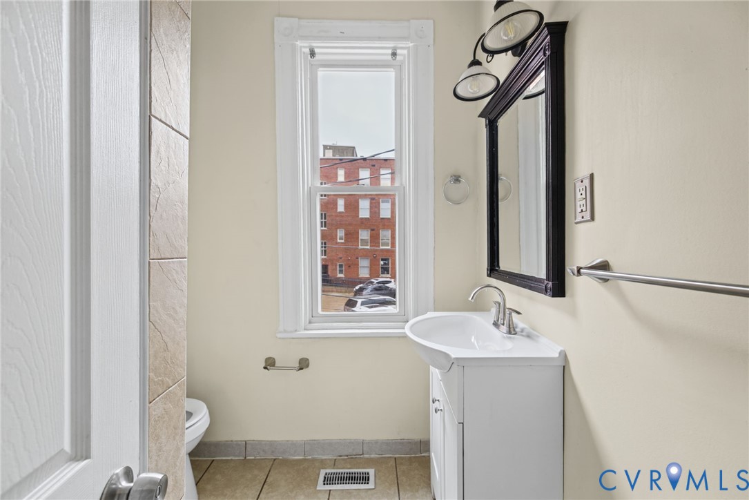 White pedestal sink with a polished chrome faucet, framed dark-finish wall mirror, multi-light fixture, and ceramic tile flooring