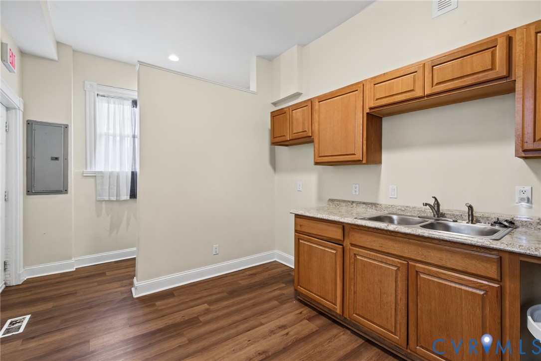 Wood-finish flooring, light-toned cabinetry, stone-finish countertops, and a dual-basin stainless steel sink