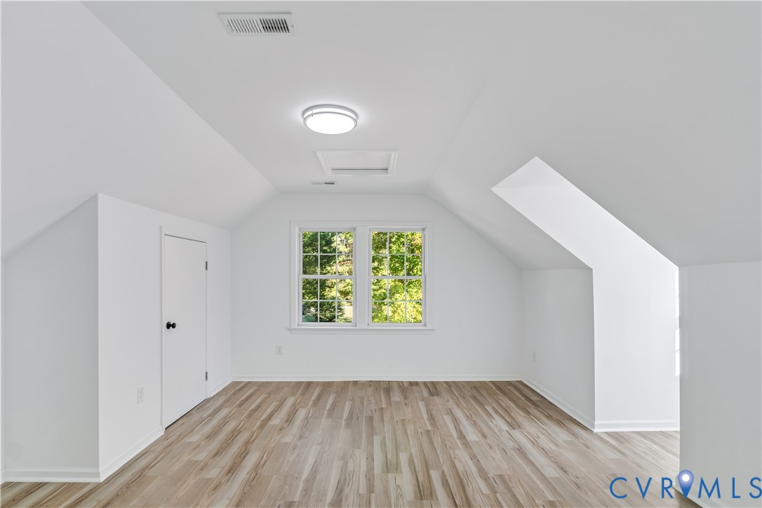 Interior space featuring wood-finish flooring, vaulted ceilings with dual-pane windows, and integrated flush-mount lighting