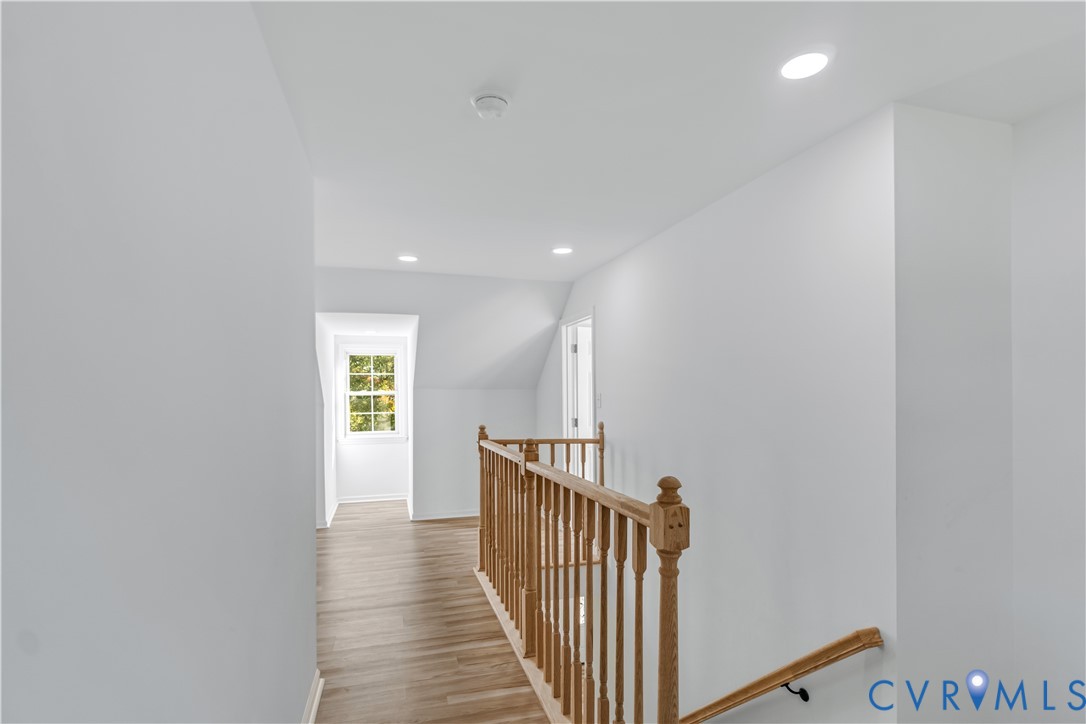Hallway featuring wood-finish flooring, recessed lighting, and a wooden balustrade with a matching handrail Hallway featuring wood-finish flooring, recessed lighting, and a wooden balustrade with a matching handrail