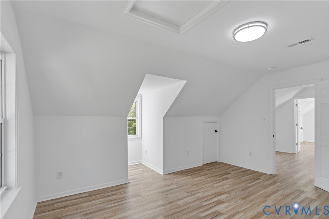 Multi-purpose room featuring sloped ceilings, wood-finish flooring, a recessed window nook, and integrated access door for storage