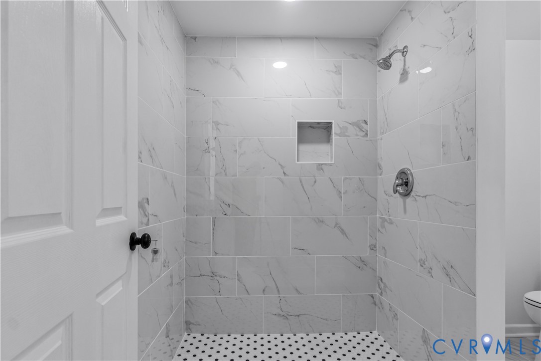Walk-in shower featuring large-format stone-patterned wall tile, white penny tile flooring, integrated wall niche, and polished chrome shower fixtures