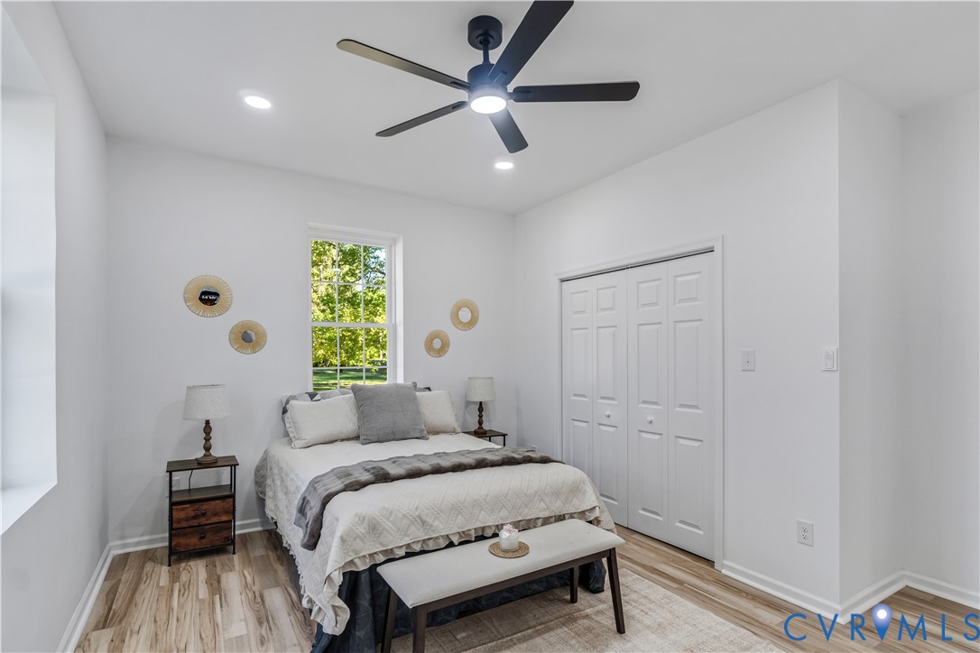 Neutral-toned interior featuring wood-finish flooring, a matte black multi-blade ceiling fan with integrated lighting, recessed lighting, and a dual-panel closet door