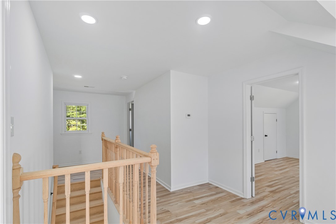 Neutral interior space featuring wood-finish flooring, recessed lighting, and a natural wood staircase railing