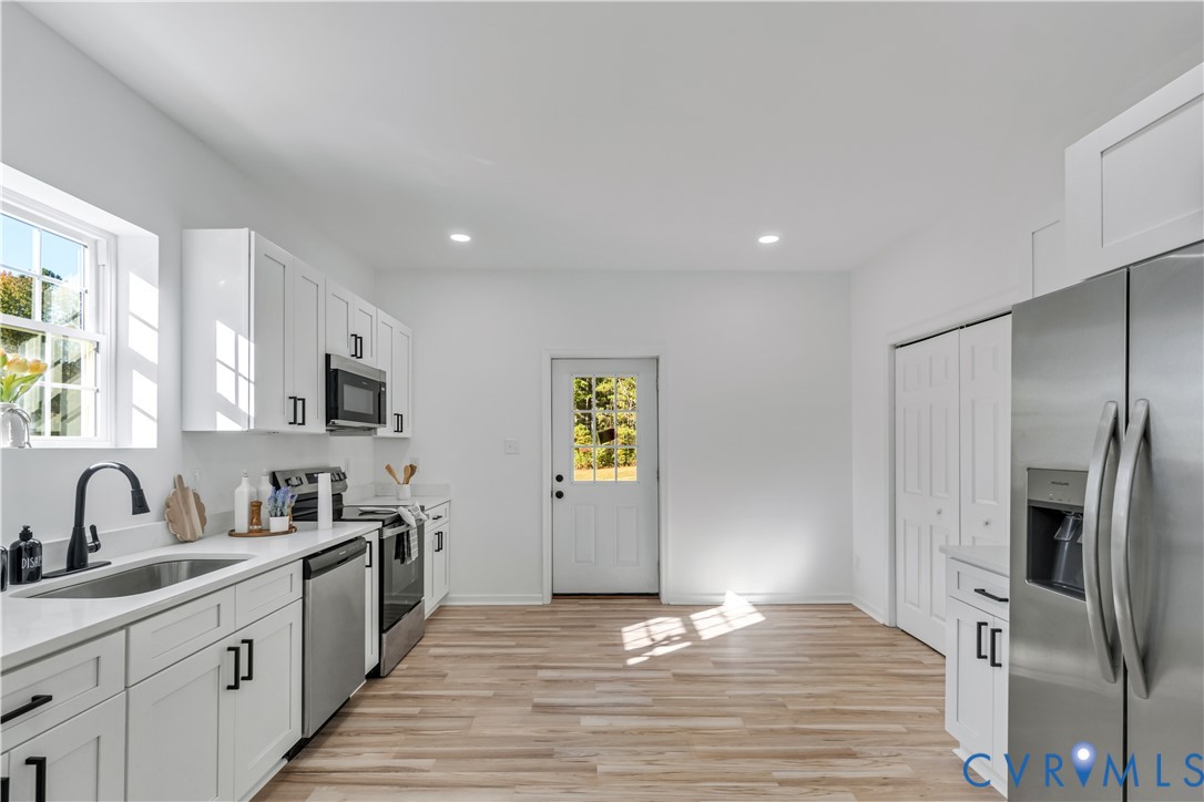 Kitchen featuring white shaker-style cabinetry, stainless steel appliances, wood-finish flooring, recessed lighting, and white countertops Kitchen featuring white shaker-style cabinetry, stainless steel appliances, wood-finish flooring, recessed lighting, and white countertops