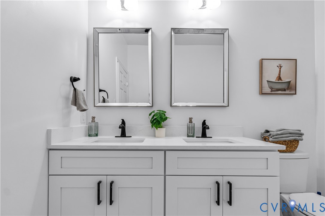 Dual-sink vanity with white shaker-style cabinetry, matte black hardware, stone-surface countertop, and two framed wall-mounted mirrors