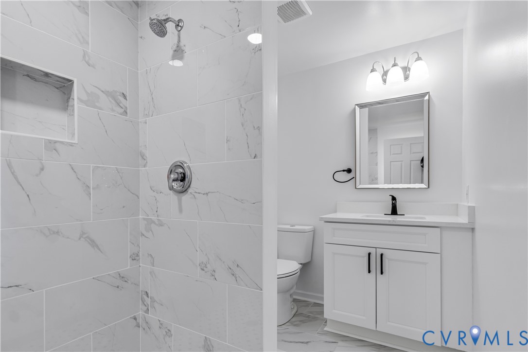 Bathroom featuring a walk-in shower with large-format stone-patterned wall tiles and a built-in shower niche, a white vanity with integrated countertop, and matte black plumbing fixtures