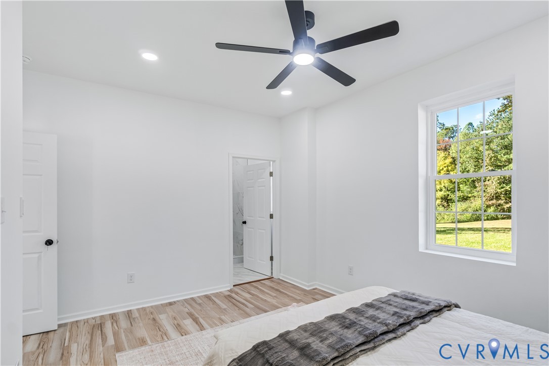 Neutral wall palette, wood-finish flooring, recessed lighting, matte black ceiling fan, and multi-pane window