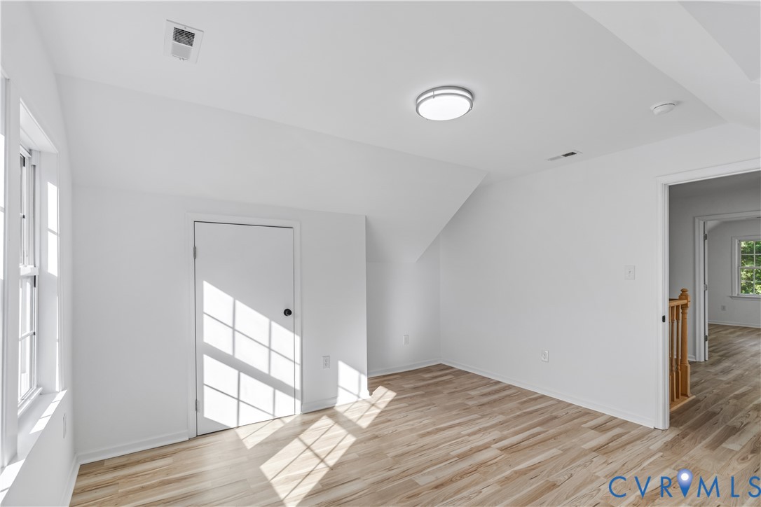 Neutral-toned room featuring sloped ceilings, wood-finish flooring, a flush-mount circular light fixture, and a single-panel interior door