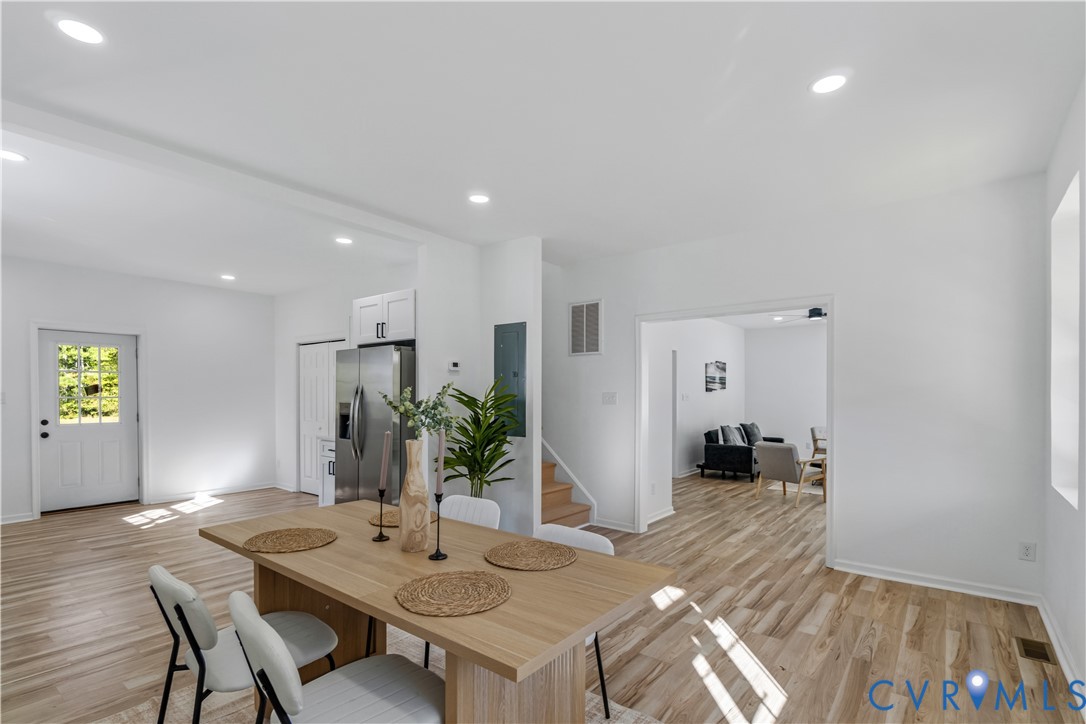 Open-concept interior featuring wood-finish flooring, recessed lighting, and a stainless steel refrigerator Open-concept interior featuring wood-finish flooring, recessed lighting, and a stainless steel refrigerator
