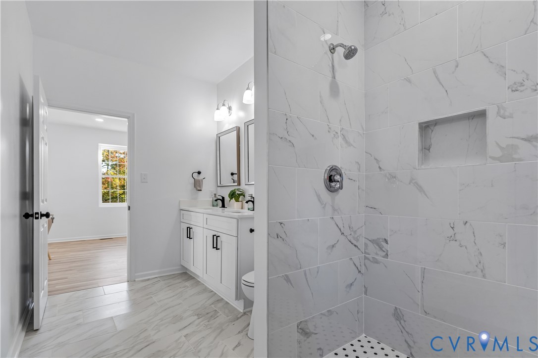 Bathroom featuring a tiled shower with a built-in niche, dual-sink vanity with cabinet storage, and light-toned flooring