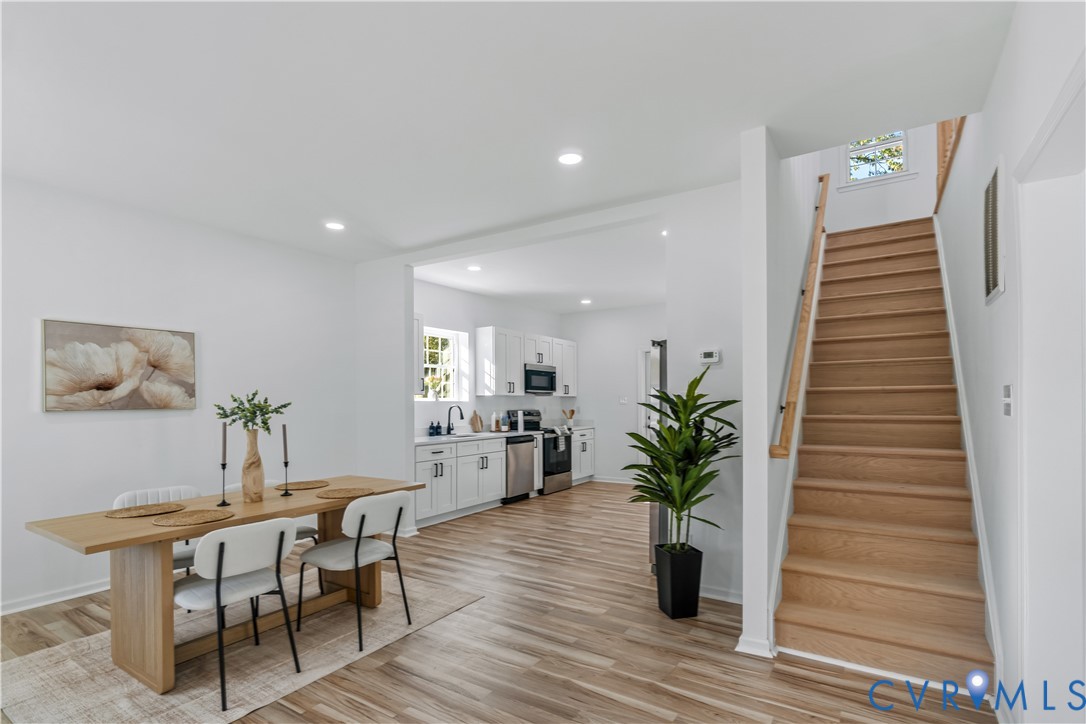 Open-concept interior featuring wood-finish flooring, recessed lighting, and a staircase with a wooden handrail Open-concept interior featuring wood-finish flooring, recessed lighting, and a staircase with a wooden handrail