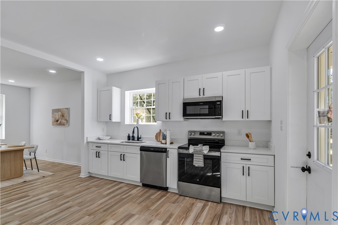 Kitchen featuring white shaker-style cabinetry, stainless steel appliances, wood-finish flooring, recessed lighting, and a matte black faucet Kitchen featuring white shaker-style cabinetry, stainless steel appliances, wood-finish flooring, recessed lighting, and a matte black faucet