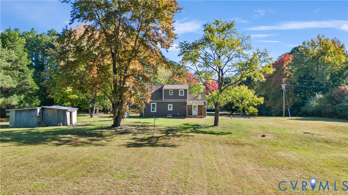 Multi-level residence featuring dark wood siding, a covered entryway, an expansive lawn, mature trees, and a detached storage structure
