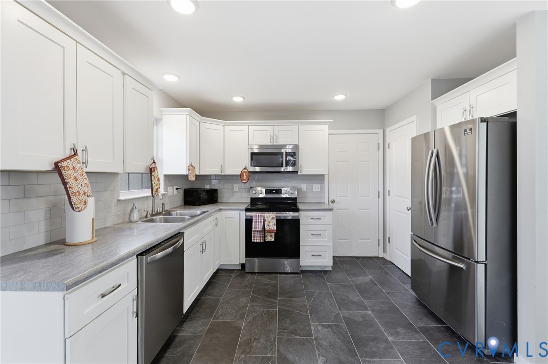 Kitchen featuring white cabinetry, grey stone-finish countertops, stainless steel appliances, a light-toned tile backsplash, and dark tile flooring