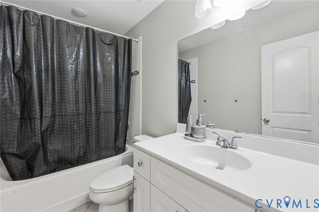 Bathroom featuring a white vanity with a composite countertop and integrated sink, a large wall-mounted mirror, a tub-shower combination, and polished chrome fixtures