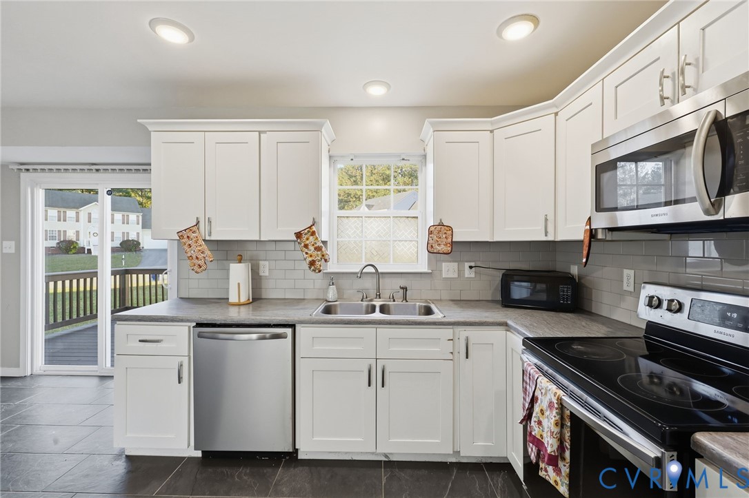 Kitchen featuring white shaker-style cabinetry, stainless steel appliances, subway tile backsplash, stone-finish countertops, and large-format floor tile