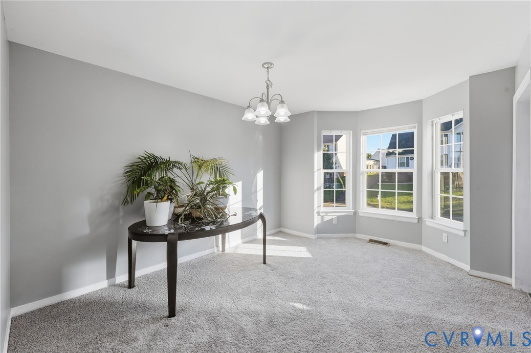 Neutral-toned interior featuring a bay window with triple-pane glazing, wall-to-wall carpeting, and a five-arm multi-light chandelier
