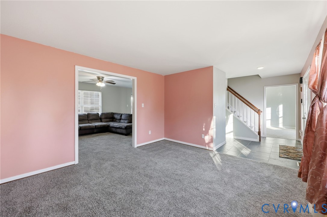 Interior room featuring wall-to-wall carpeting, painted walls, tile flooring in the entry area, and a staircase with a wooden handrail and balusters