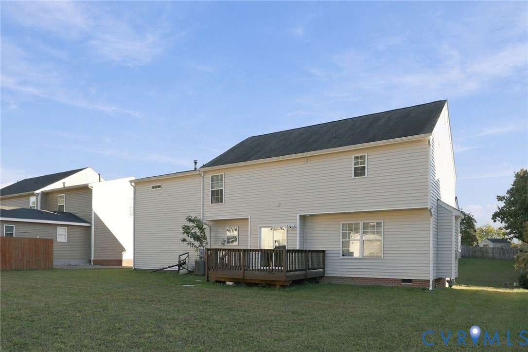 Two-story exterior featuring light-colored horizontal siding, a pitched shingle roof, a raised wooden deck, and a spacious backyard