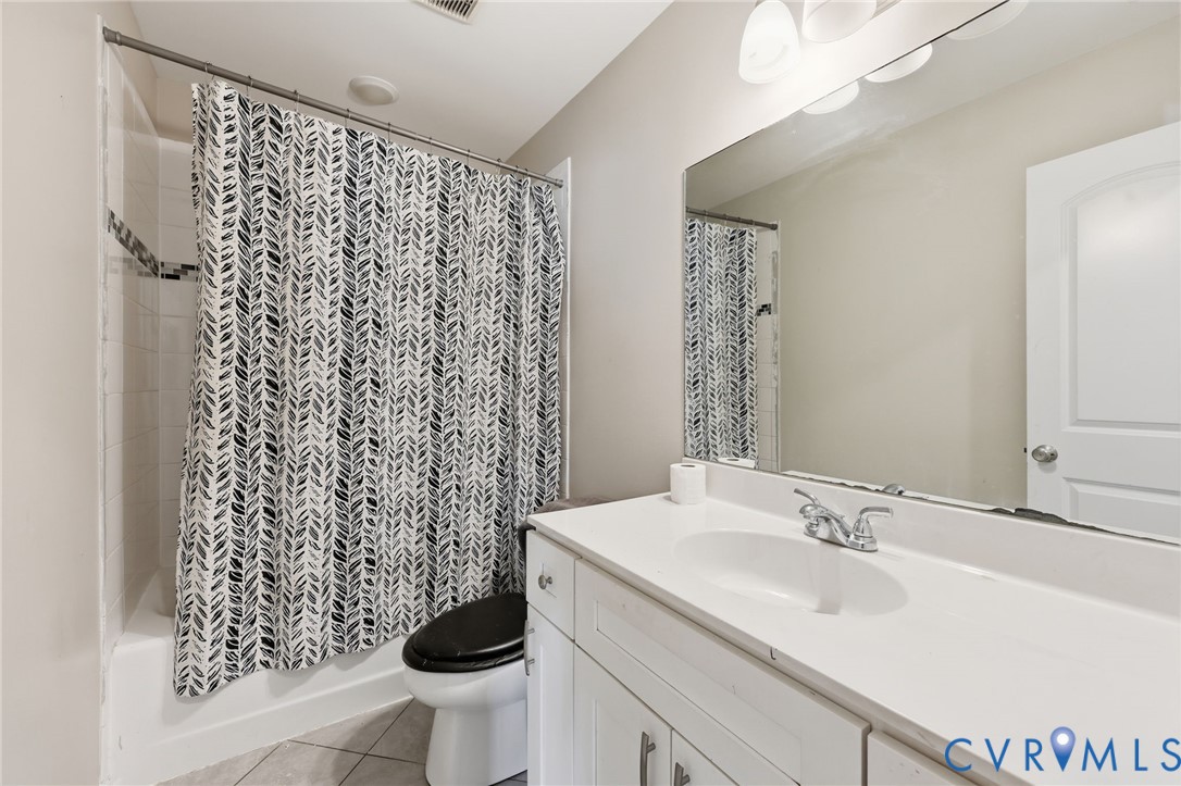 Full-width vanity with white cabinetry and integrated sink, large wall-mounted mirror, tub-shower combination with tile surround, and tile flooring