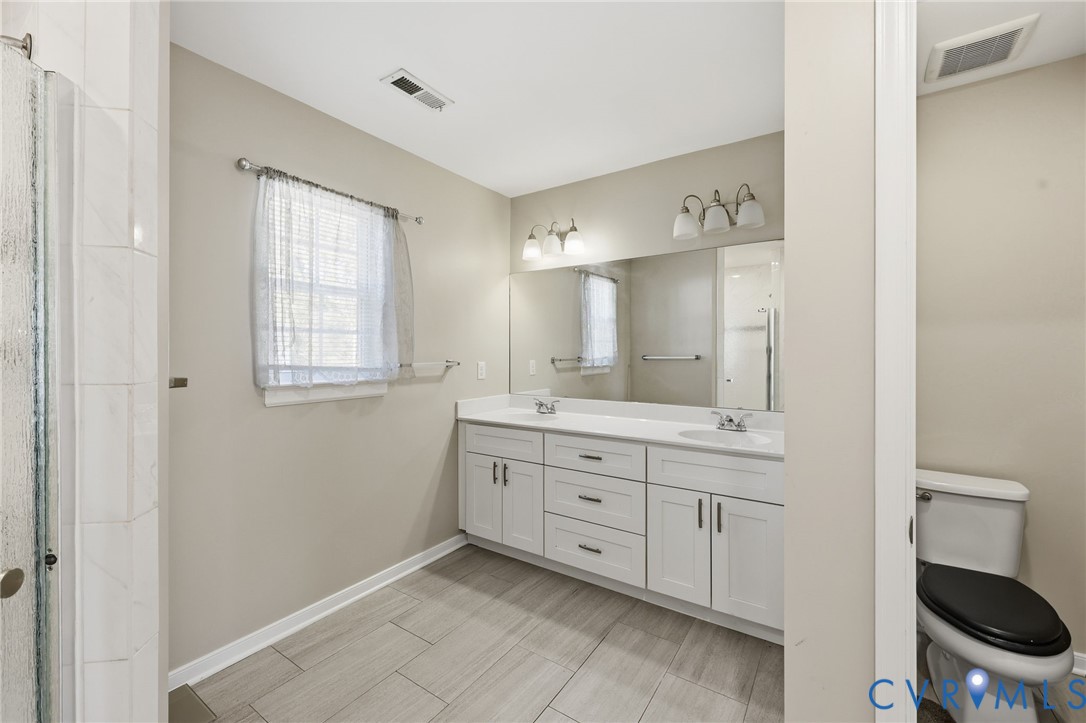 Double vanity with white cabinetry, solid surface countertop, tile flooring, and wall-mounted light fixtures