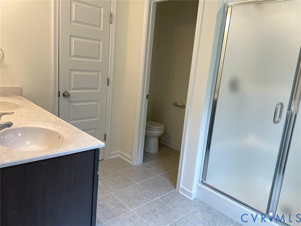 Bathroom featuring tile patterned floors, toilet, a shower with door, and vanity