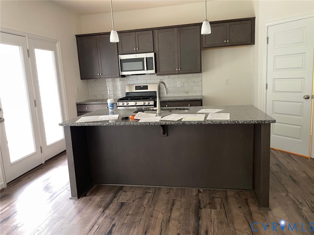 Kitchen with appliances with stainless steel finishes, dark wood-type flooring, and dark stone counters